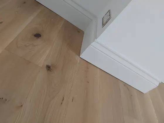Close-up of new white skirting board meeting an oak floor neatly at an external corner